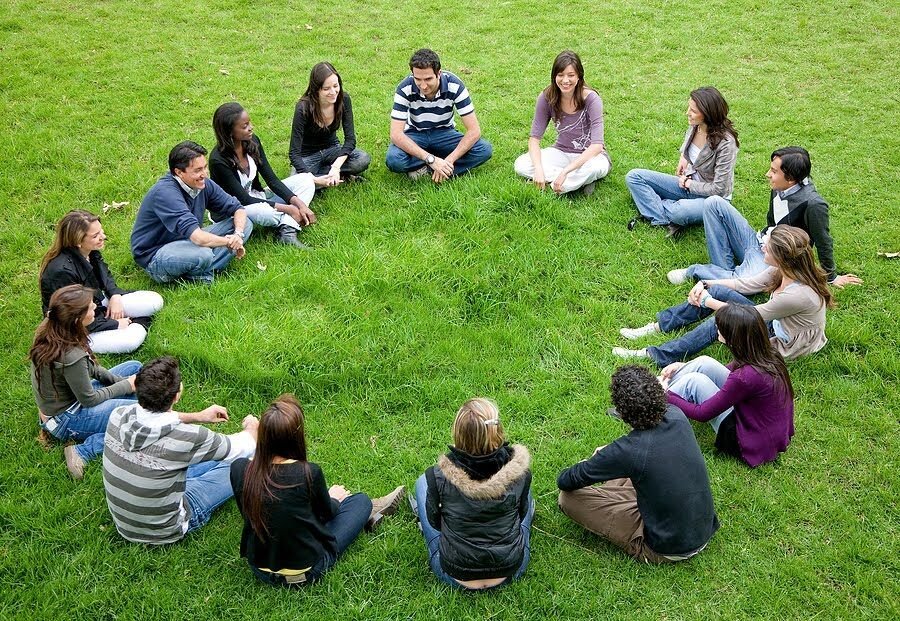Un groupe assis en cercle dans l'herbe, en pleine discussion